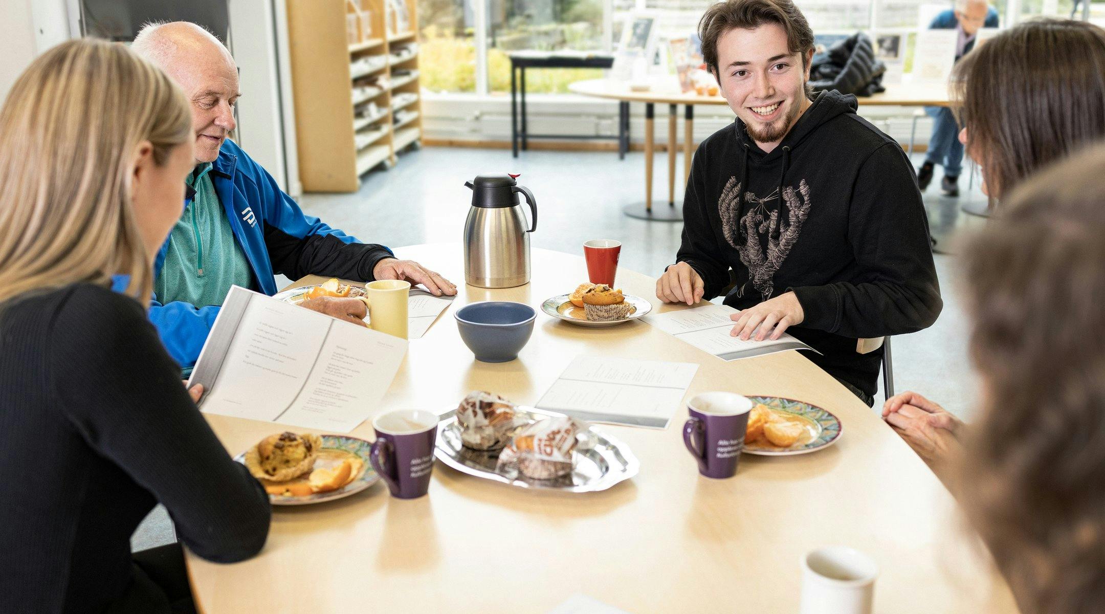 Fem personar sitt rundt eit bord med tekstar og kaffimat